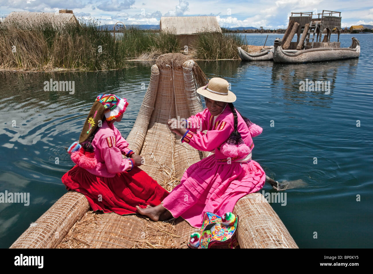 Pérou, deux fille d'Uros ramer un bateau de roseau à l'une des îles flottantes uniques du Lac Titicaca. Banque D'Images