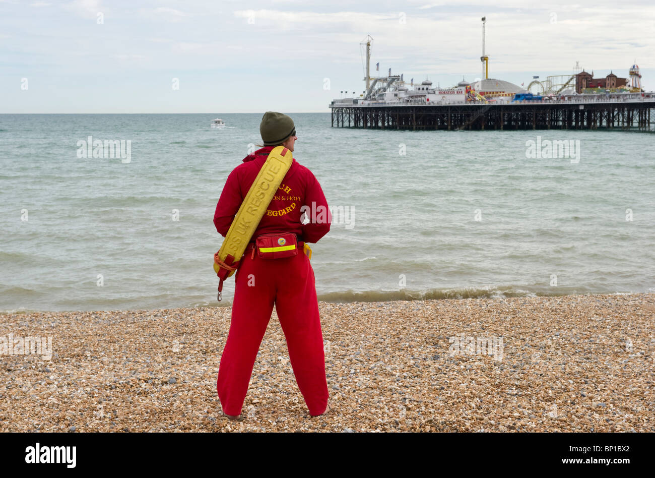 Un homme plage surveillée en service à Brighton plage de galets avec Brighton Pier dans la distance Sussex UK Banque D'Images