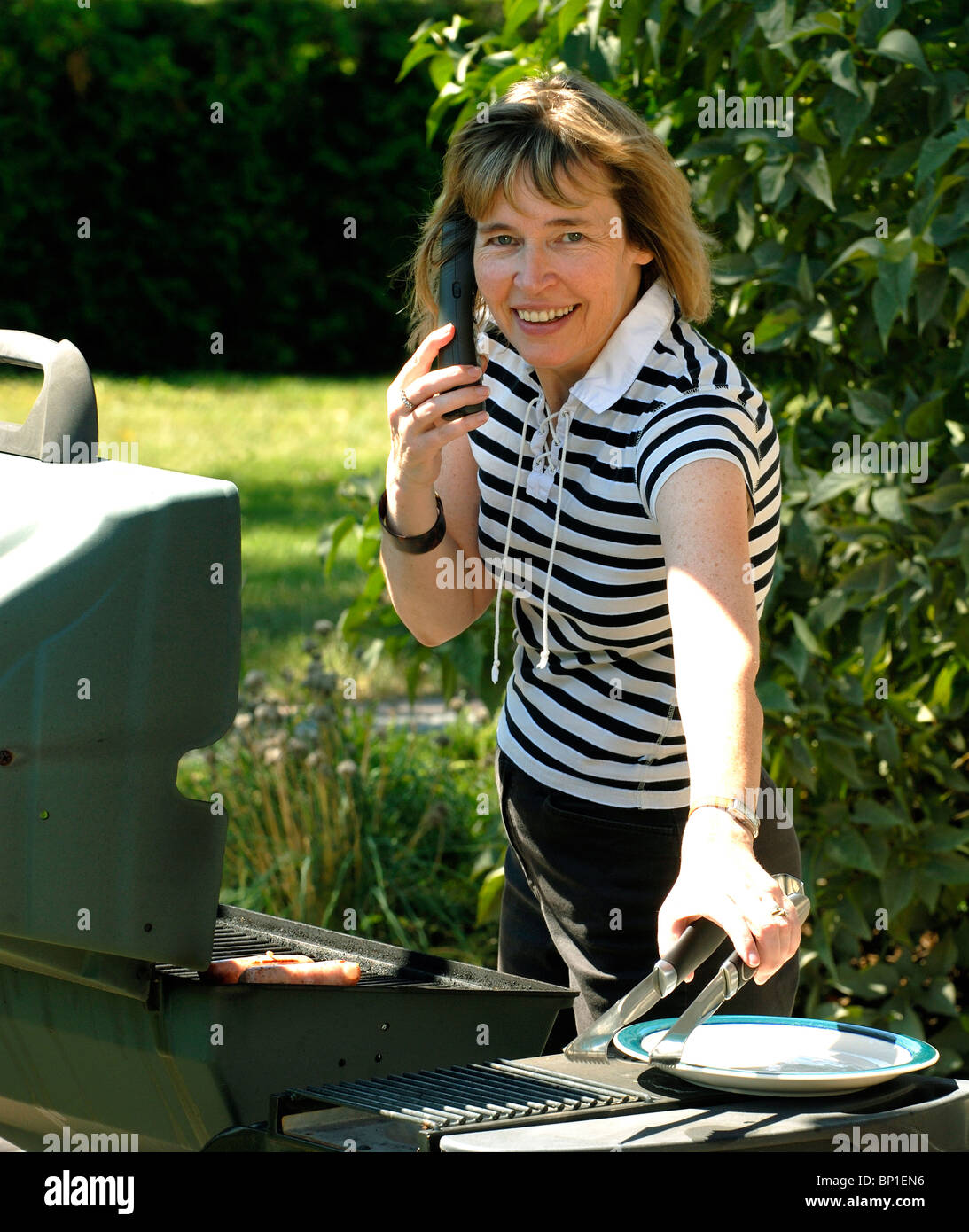 Belle Femme d'âge moyen cuisson sur un barbecue à gaz à l'extérieur en été Banque D'Images