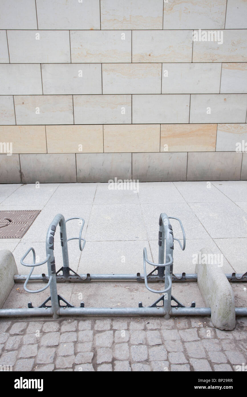 Porte-vélos urbain vide sur un trottoir avec des pavés et un mur carrelé beige en arrière-plan. Banque D'Images