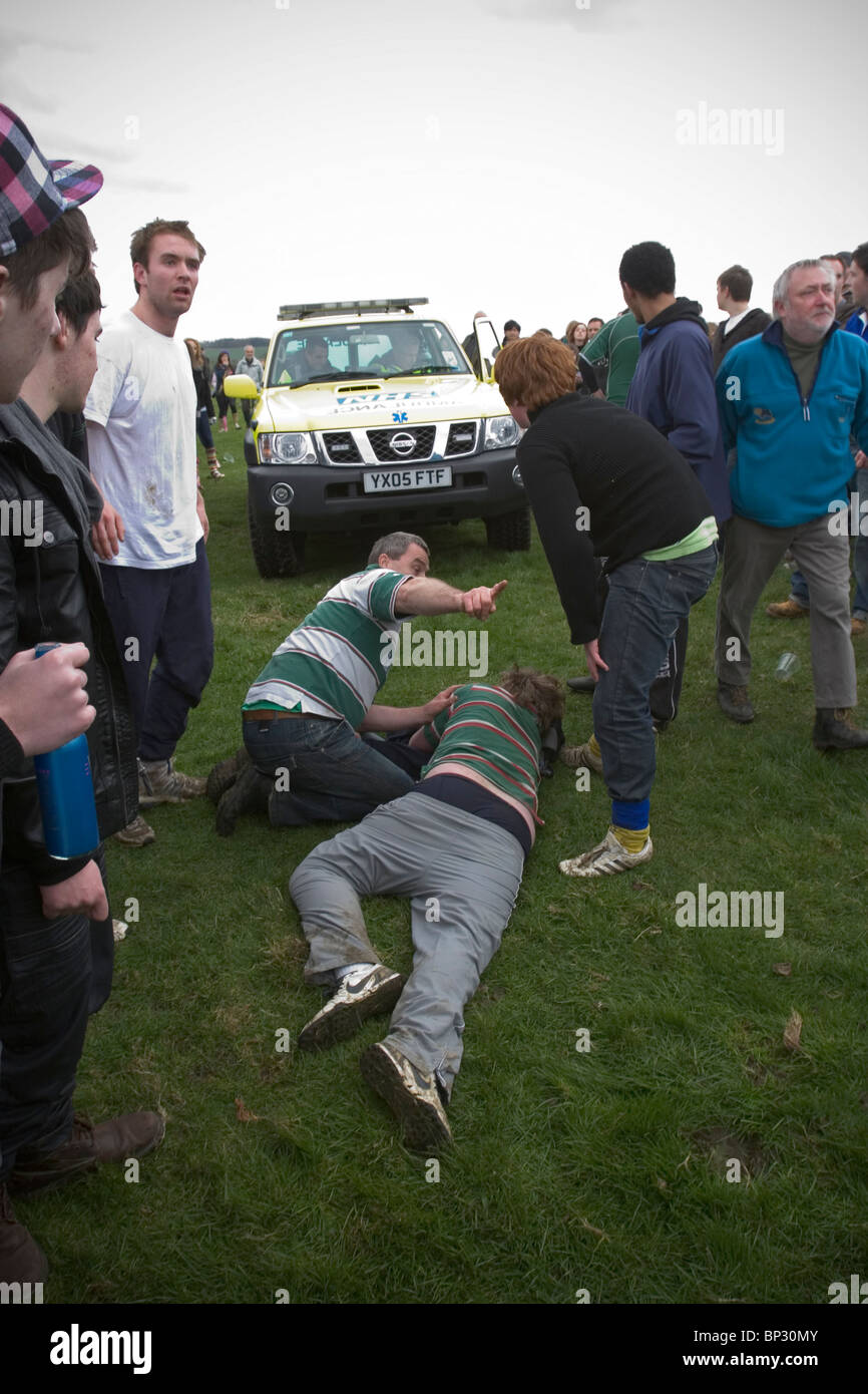 Homme étendu sur le sol en attente de soins médicaux après avoir été foulés au cours de jeu traditionnel de Bottlekicking, Leicestershire, UK Banque D'Images