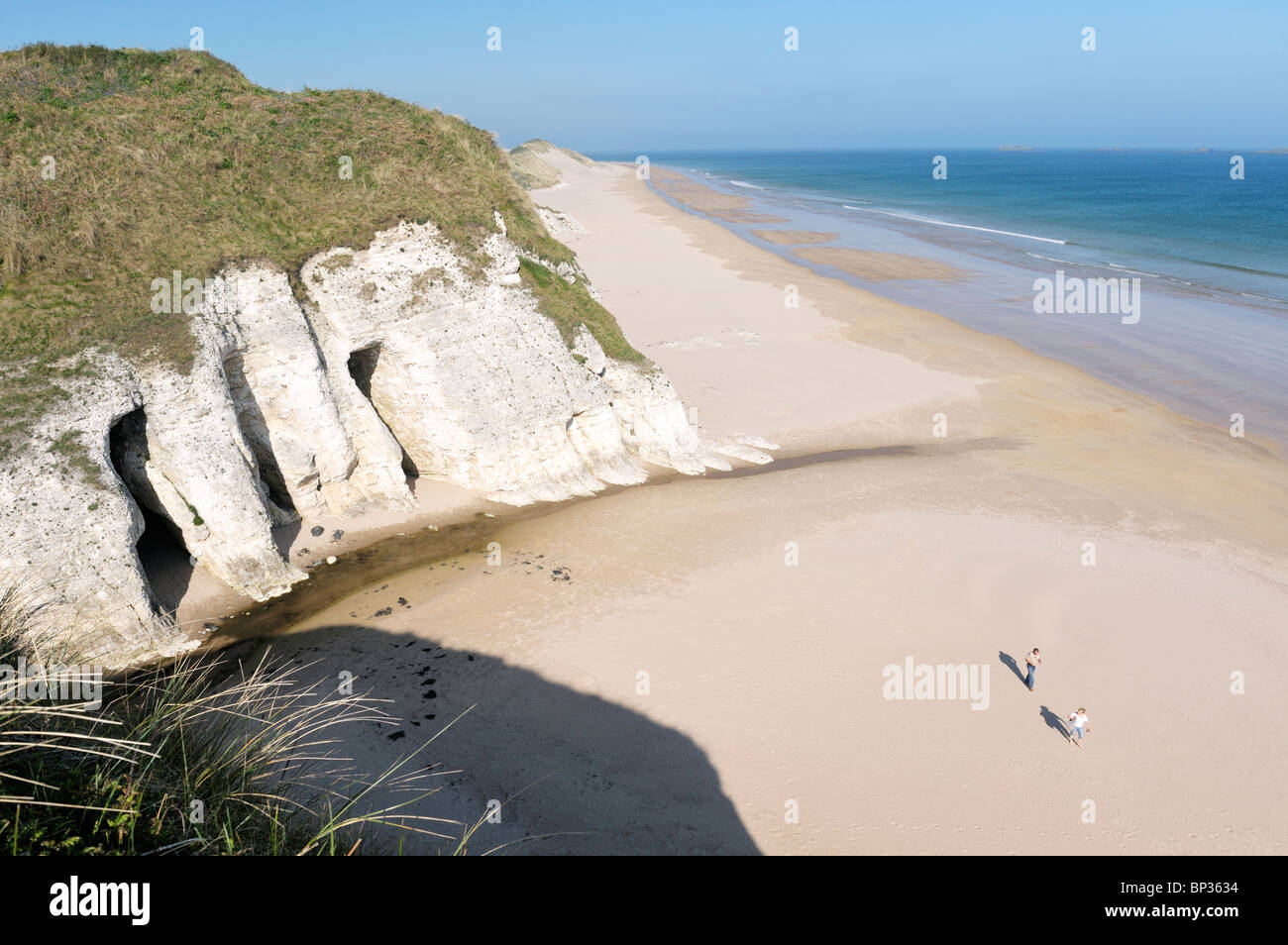 Couple en train de marcher sur la plage déserte à la Roche Blanche entre Portrush et Bushmills, Irlande du Nord. Falaises de calcaire érodé Banque D'Images
