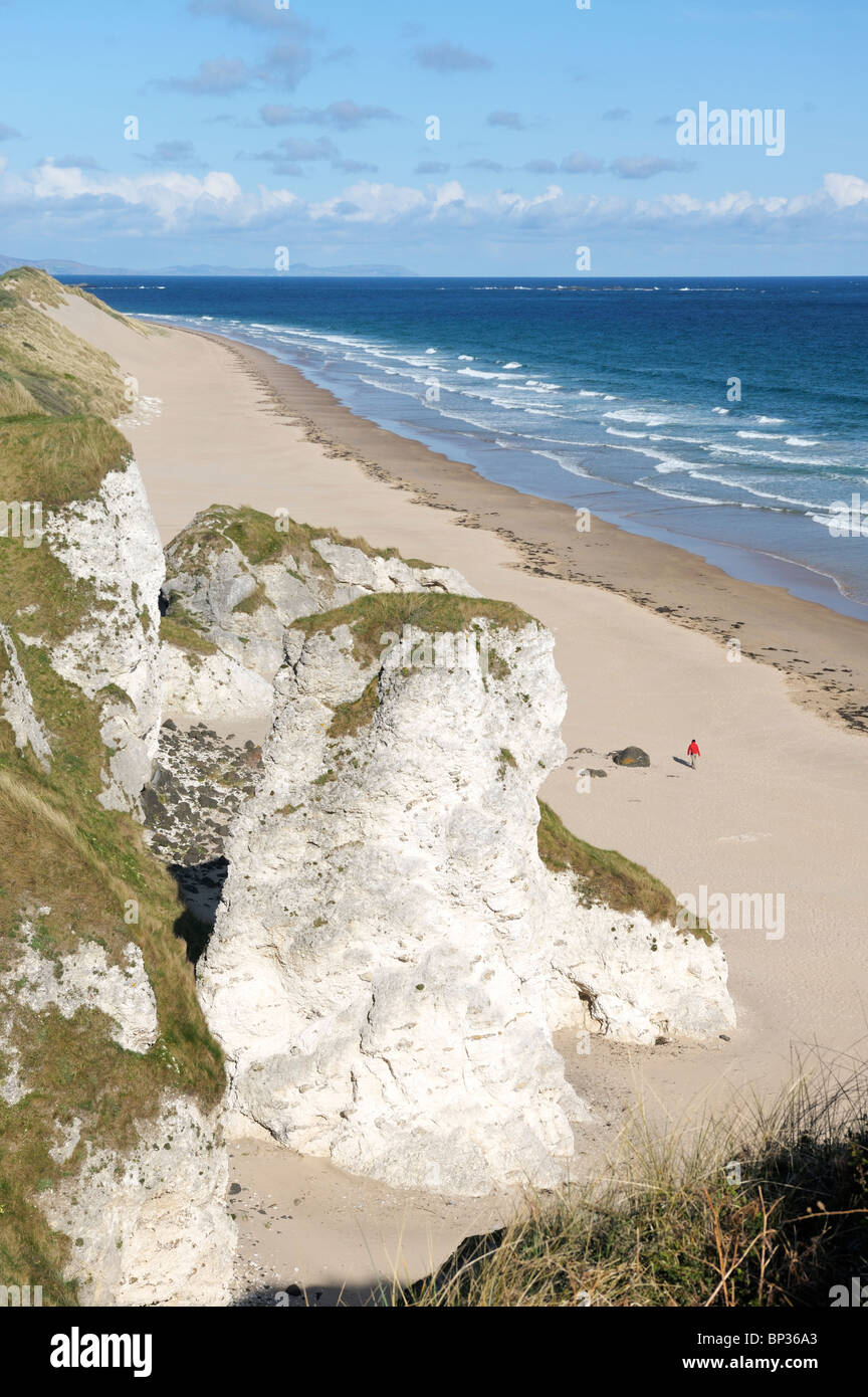 Jeune femme marcher seule sur la plage de White Rocks entre Portrush et Bushmills, Irlande du Nord. Falaises de calcaire érodé Banque D'Images