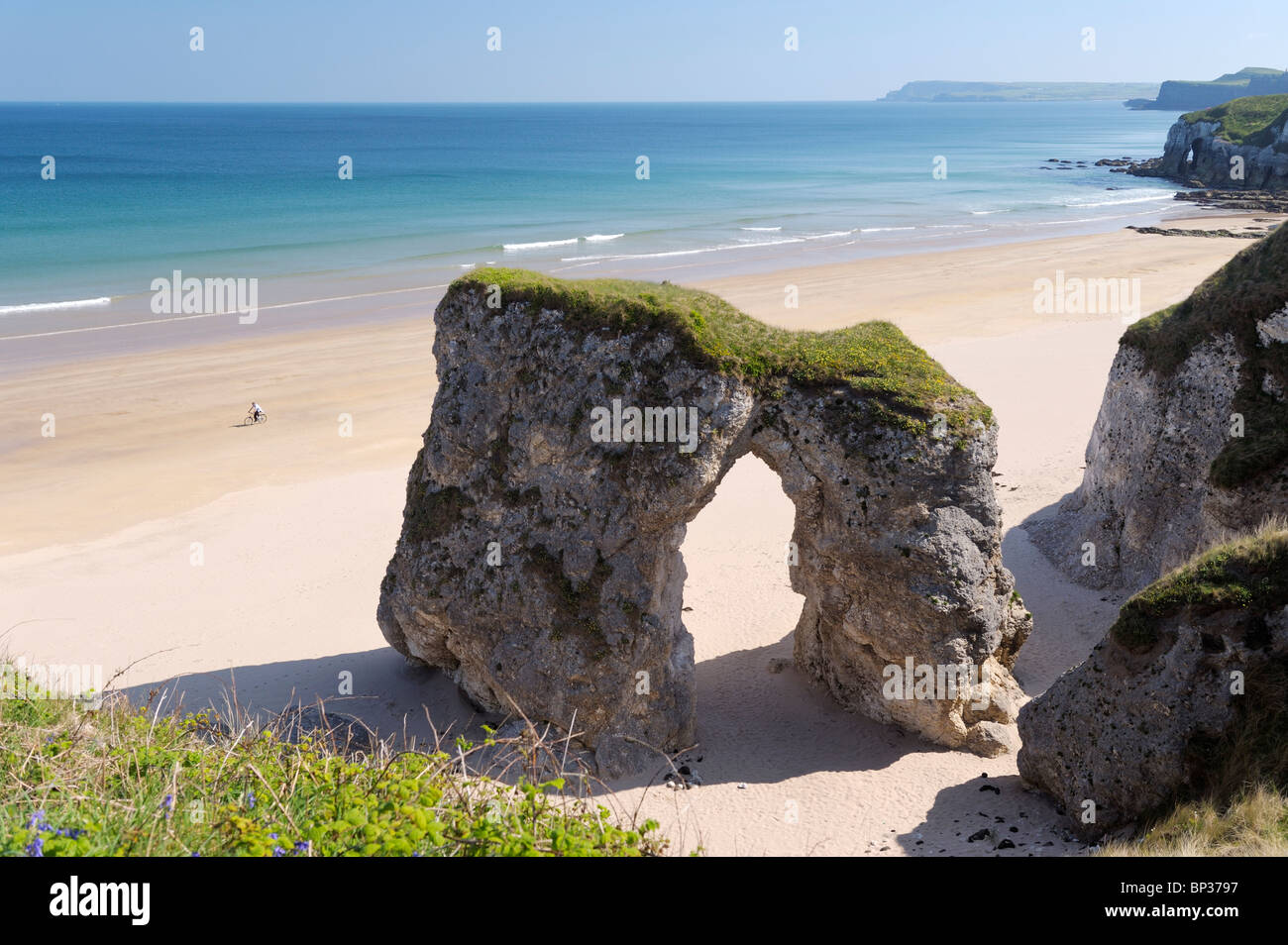 Man riding bicycle sur plage déserte au White Rocks entre Portrush et Bushmills, Irlande du Nord. Falaise calcaire érodé Banque D'Images