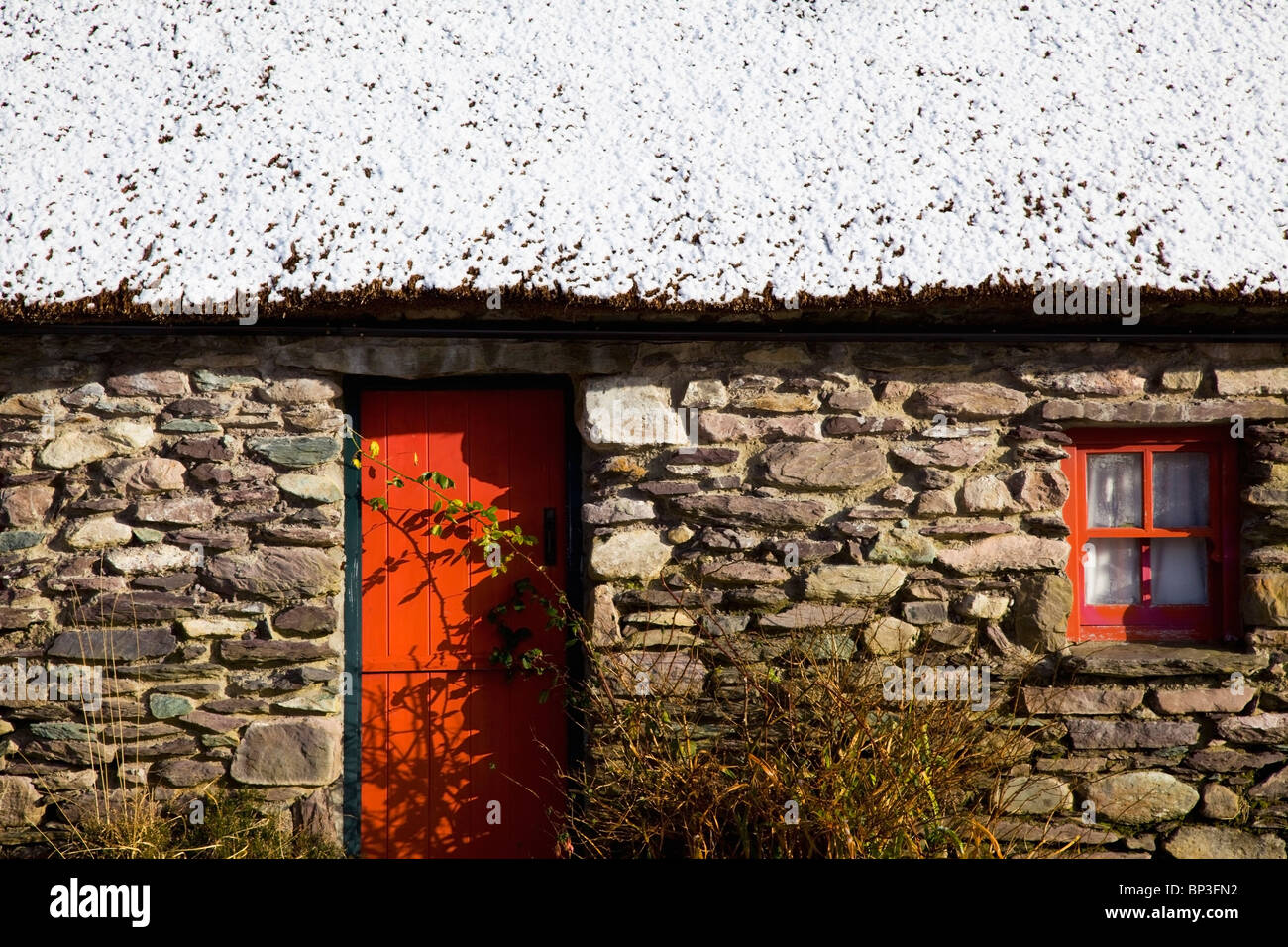 Bonane, comté de Kerry, Irlande ; une maison en pierre avec une porte orange et le cadre de la fenêtre et la neige sur le toit Banque D'Images