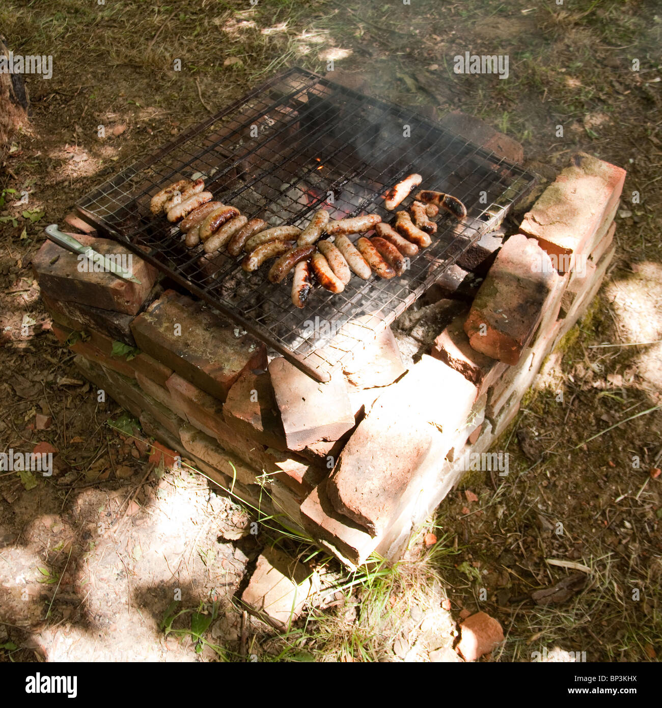 La cuisson des saucisses sur un feu de charbon ou barbecue. Hampshire, Angleterre, Royaume-Uni Banque D'Images