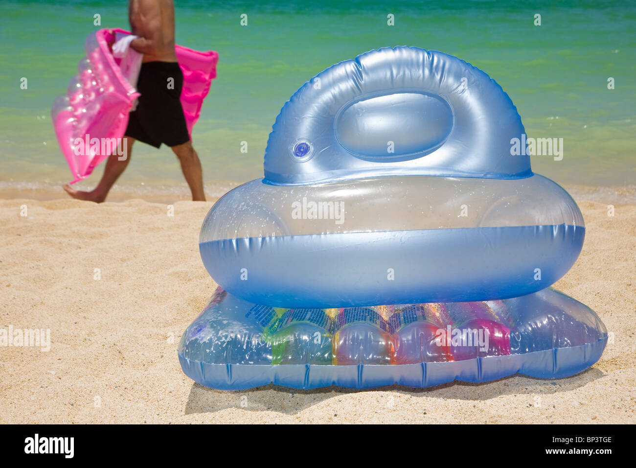 Homme marchant passé une chaise gonflable sur une belle plage Banque D'Images