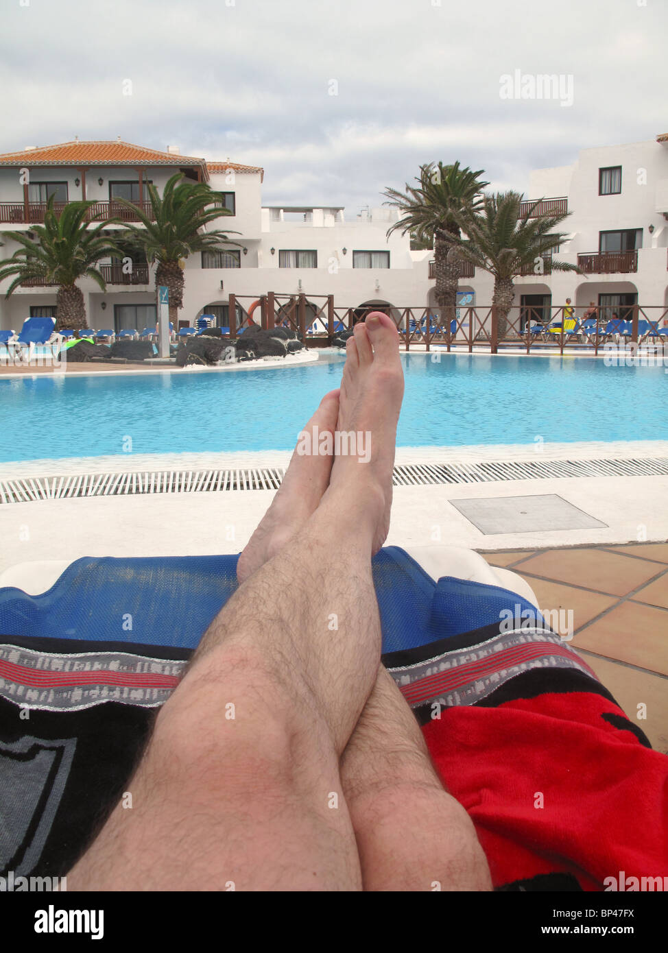 Mans pieds sur chaise longue près de la piscine Banque D'Images