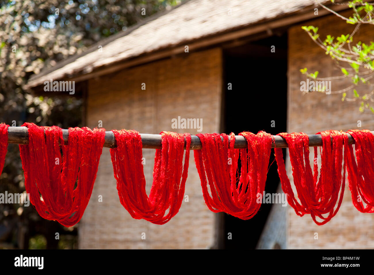 Fils de soie teints en rouge sur un poteau de séchage à l'extérieur d'une cabane en bambou - Province de Kandal, Cambodge Banque D'Images