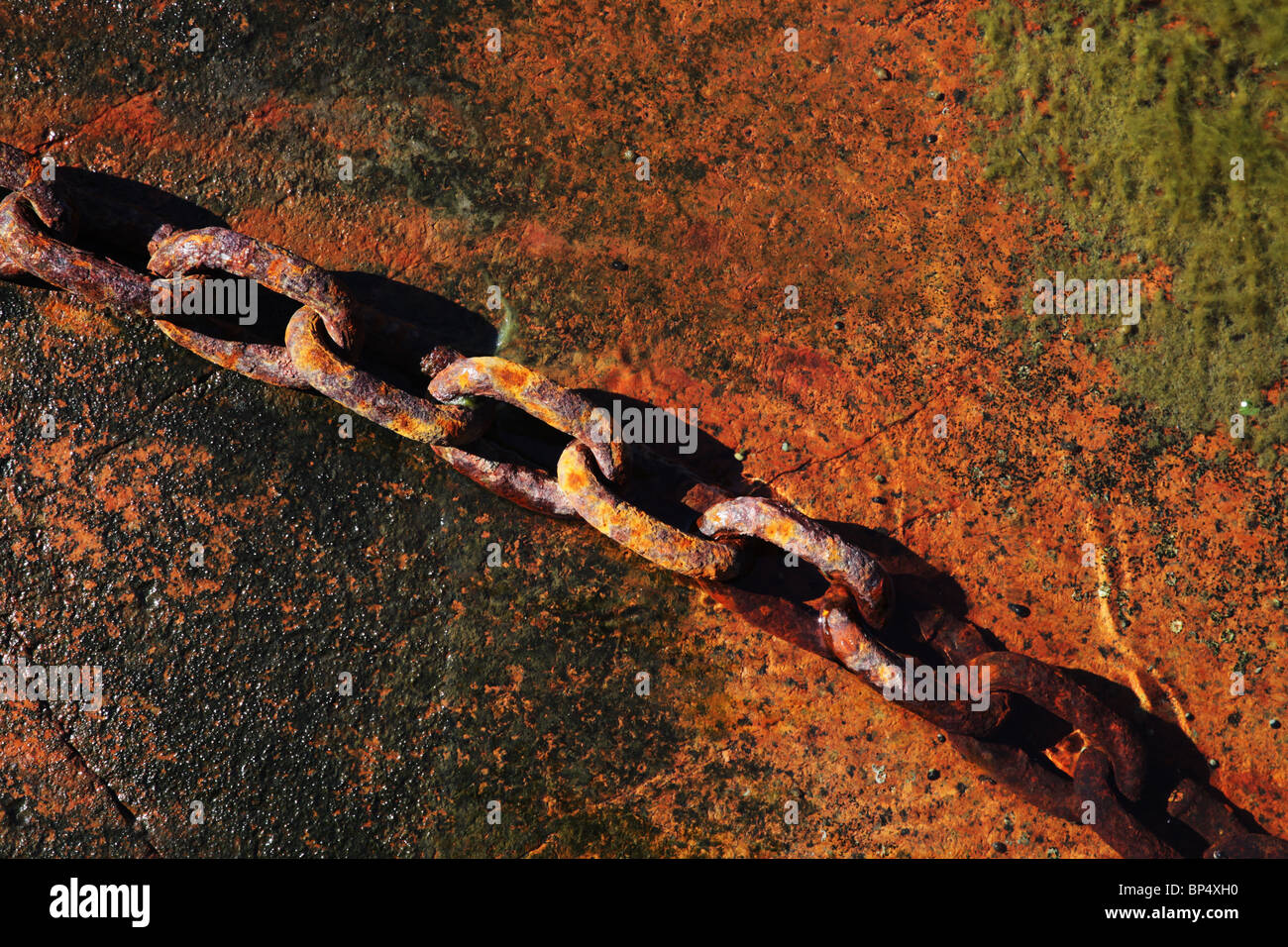 Liens de la chaîne de fer rouille reposant sur red rock et dans l'eau au bord de la mer Banque D'Images