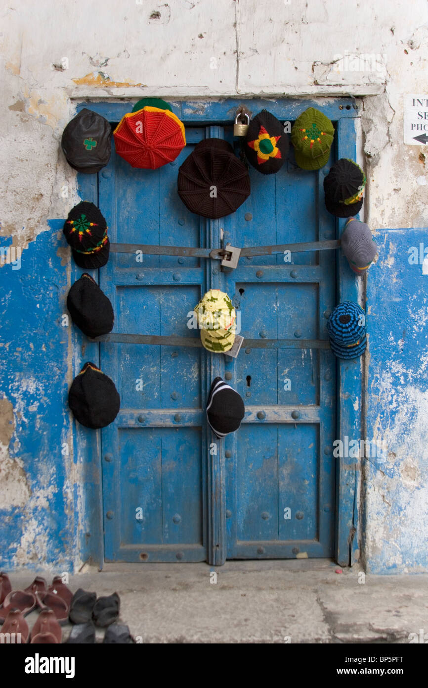 Chapeaux colorés et à la vente de l'EAPV, suspendu à une porte bleue à Stone Town, Zanzibar, Tanzanie Banque D'Images
