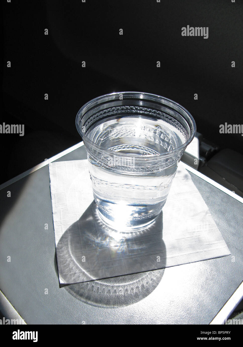 Une tasse en plastique rempli d'eau sur une serviette blanche sur un avion du conducteur bac avec une forte lumière de la fenêtre. Banque D'Images