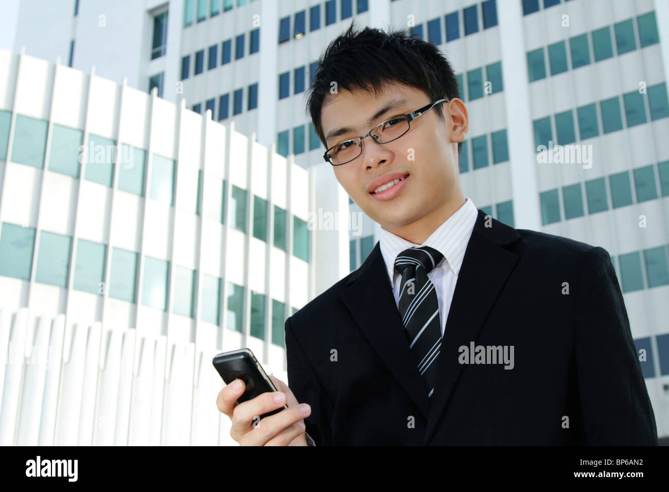 Un jeune chef d'entreprise asiatique en utilisant son téléphone cellulaire en face d'un immeuble de bureaux Banque D'Images