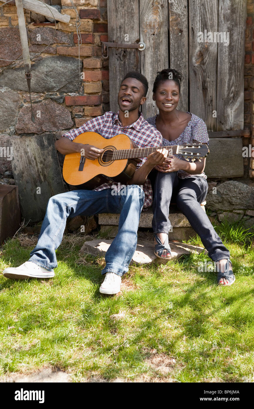 Un homme jouant de la guitare acoustique et le chant avec sa petite amie Banque D'Images