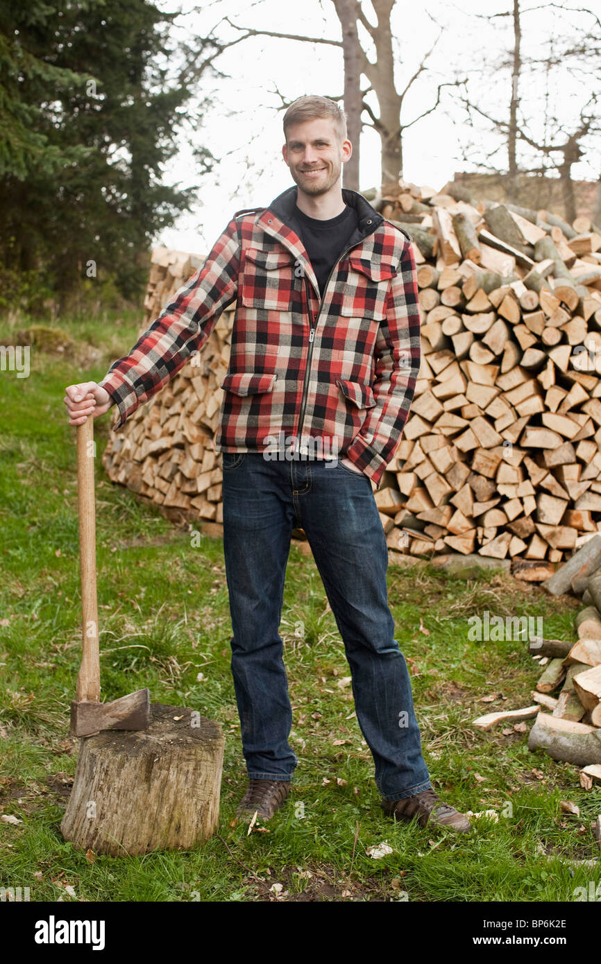 Un homme tenant une hache, debout devant un tas de bois Banque D'Images
