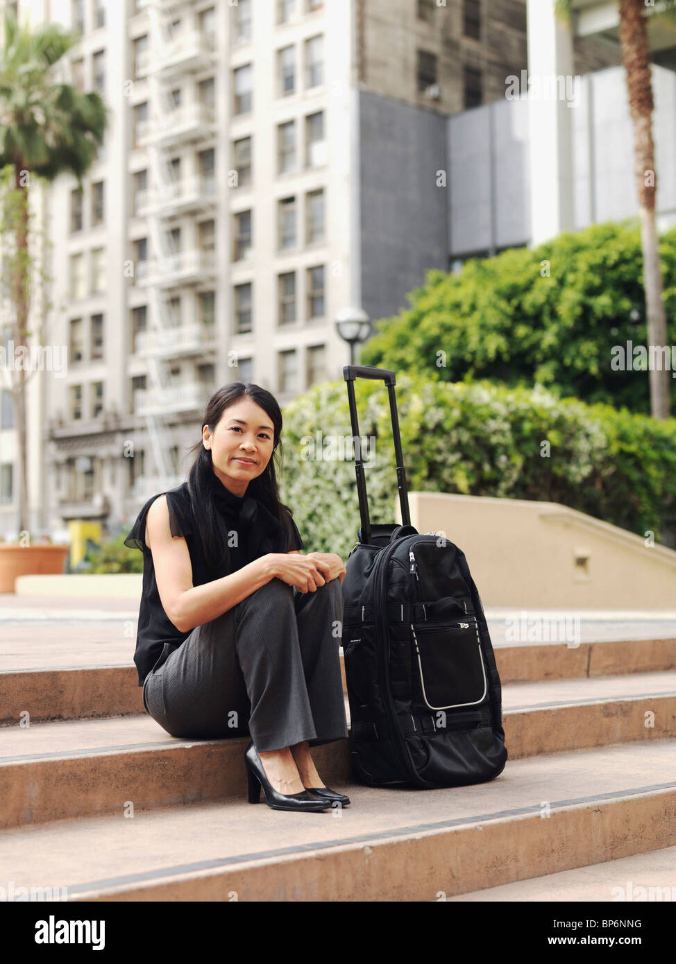 Une femme assise sur un pas à côté d'un rolling suitcase Banque D'Images