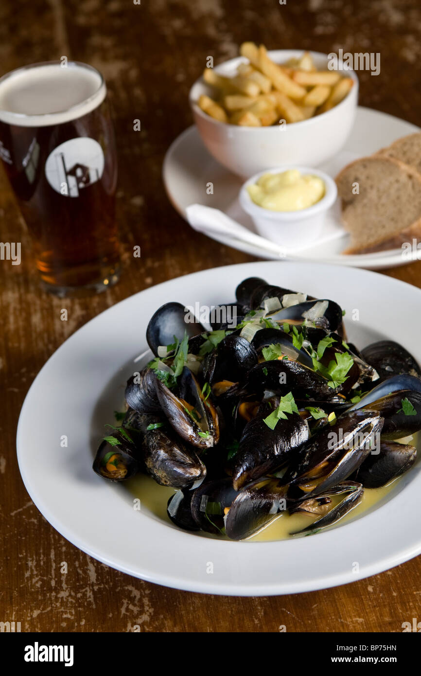 Moules marinière avec des frites et une pinte de bière sur une table de pub Banque D'Images