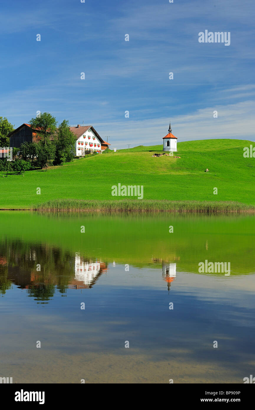 Reflet de la ferme traditionnelle bavaroise et chapelle sur le lac, de l'Allgaeu, Bavaria, Germany Banque D'Images