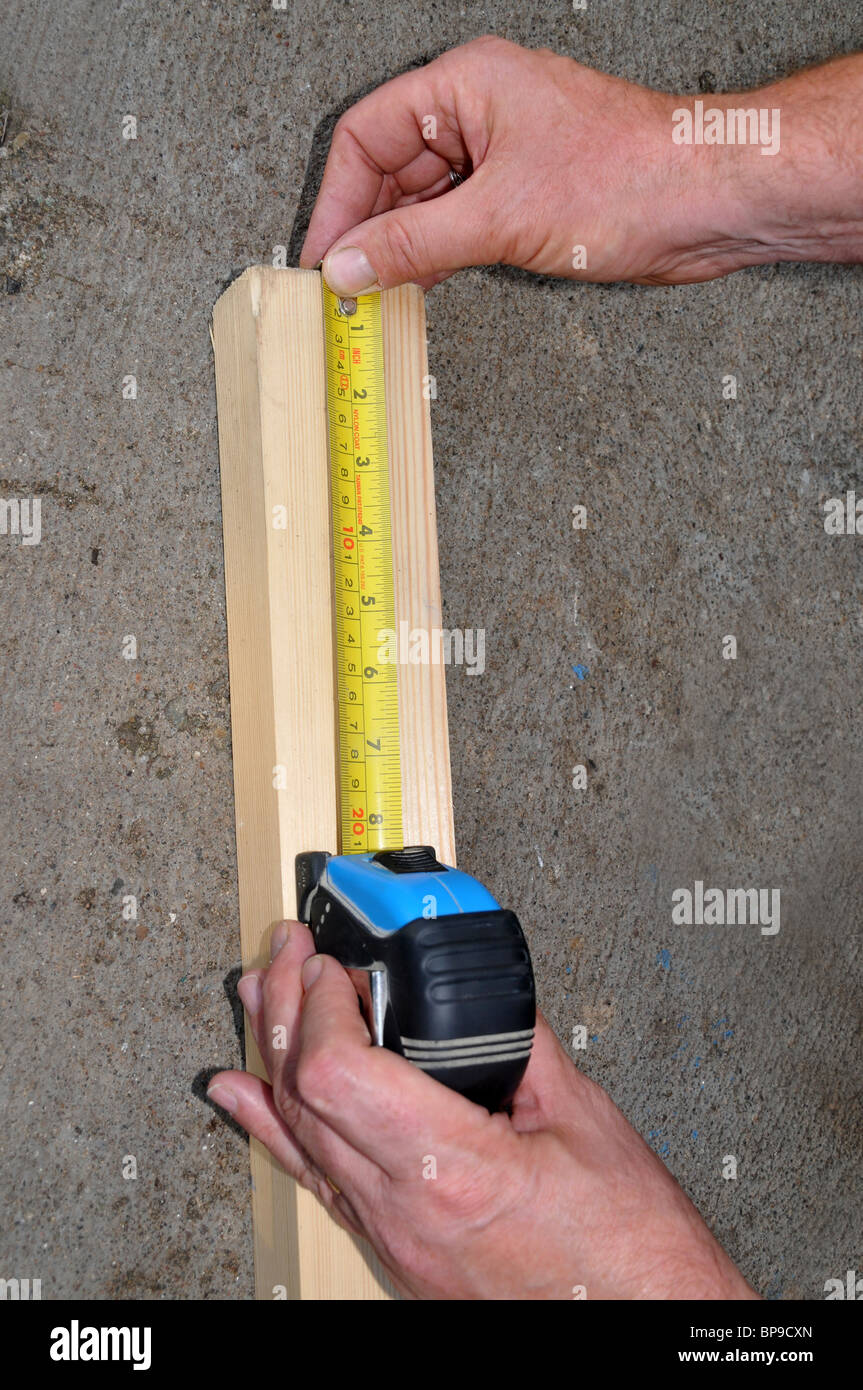 Un homme mesure un morceau de bois à l'aide d'un charpentier ruban à mesurer. Banque D'Images