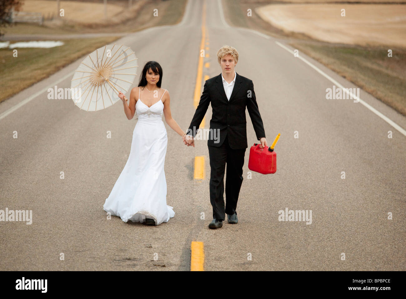 Three Hills, Alberta, Canada ; une femme et un homme marchant sur un chemin rural tenant un jerricane et un parasol Banque D'Images