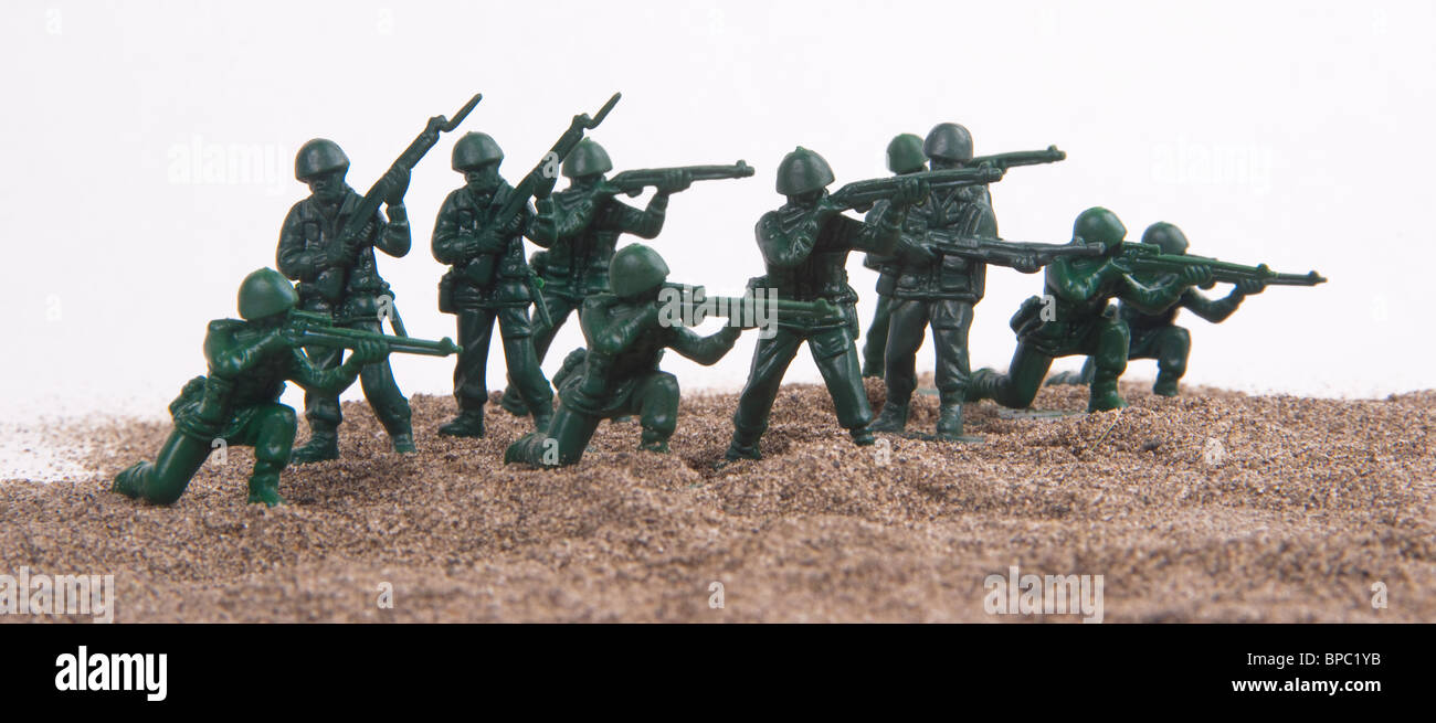 Un groupe de petits hommes de l'armée verte en plastique mis en place sur un sable sur un fond blanc. Banque D'Images