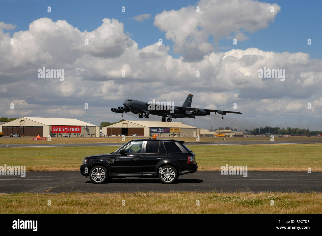 La Range Rover 4x4 automobile attend de traverser la piste en direct alors qu'un américain B52 bombardier lourd atterrit à l 2010 RIAT Banque D'Images