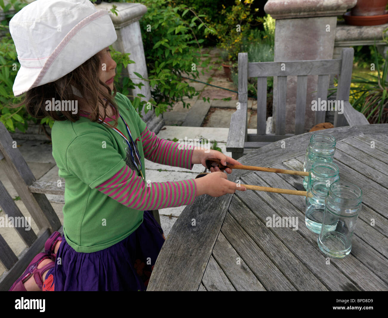 Jeune fille de faire de la musique à l'aide de pots de verre plein d'eau et de les frapper avec des cuillères en bois Banque D'Images