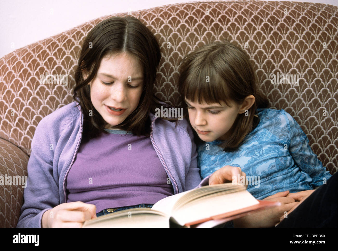 Fille de lire un livre à haute voix à sa plus jeune soeur. Banque D'Images