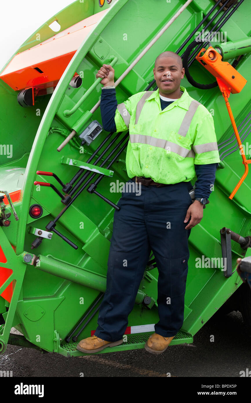 Homme noir à cheval sur l'arrière de camion poubelle Banque D'Images