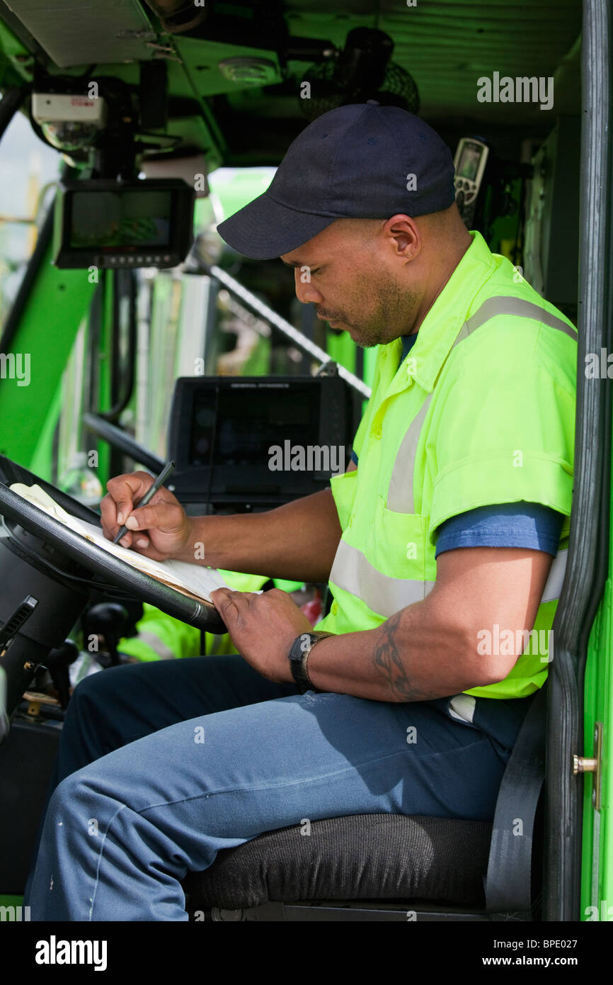 African American man in garbage truck writing on clipboard Banque D'Images