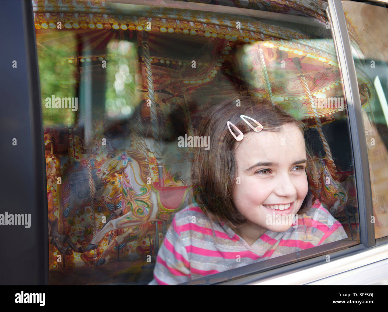 Girl smiling et regardant par la fenêtre de la voiture au parc d'ride avec la réflexion de carrousel dans verre Banque D'Images