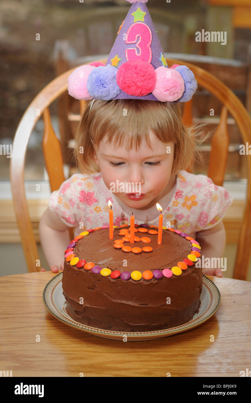 Girl célèbre sa 3e anniversaire par blowing out candles sur un gâteau au chocolat Banque D'Images