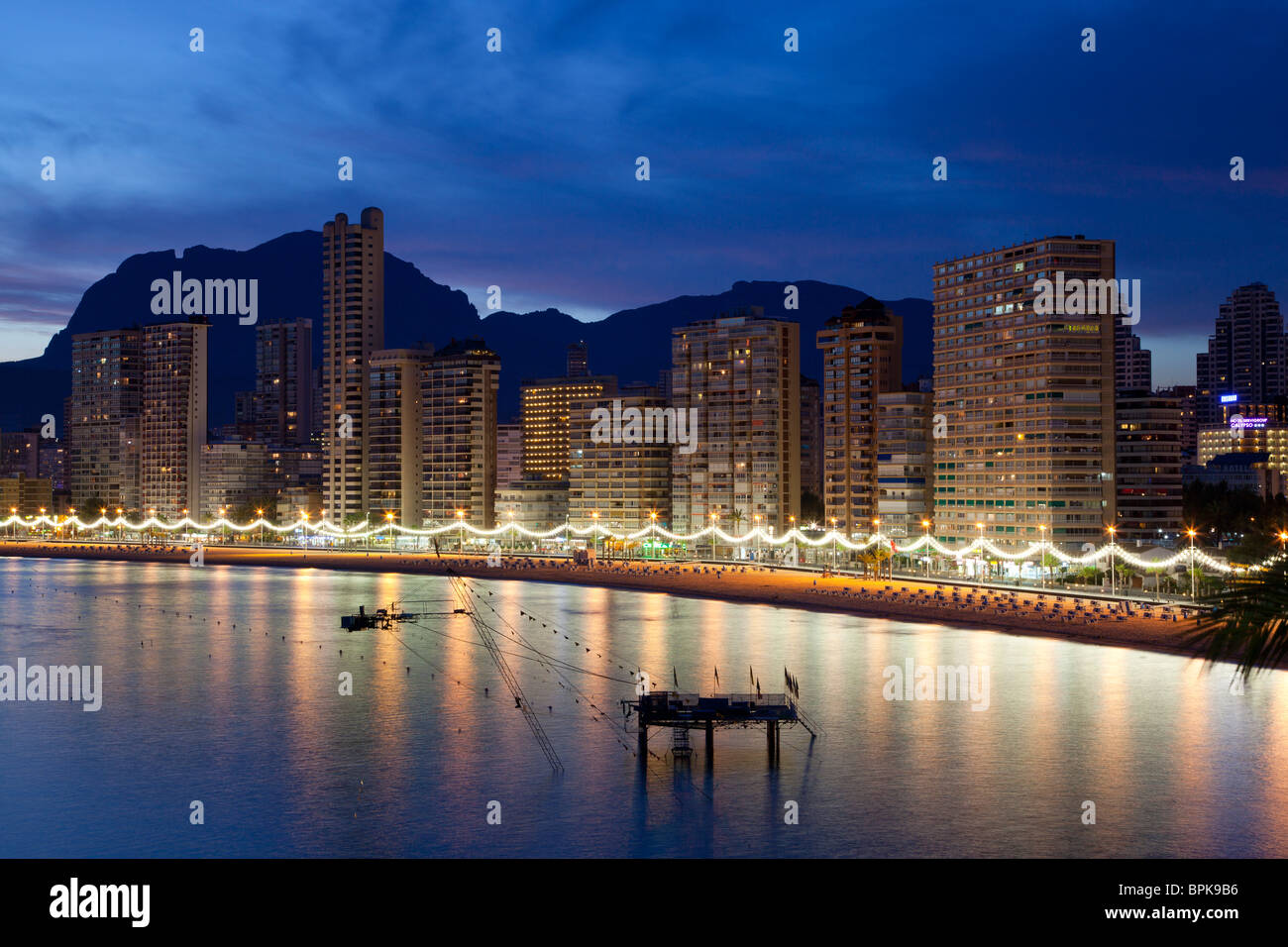 La plage Levante de Benidorm attrayant au crépuscule, avec ses bâtiments et promenade éclairés se reflétant dans la mer, montagnes Aitana  + Banque D'Images