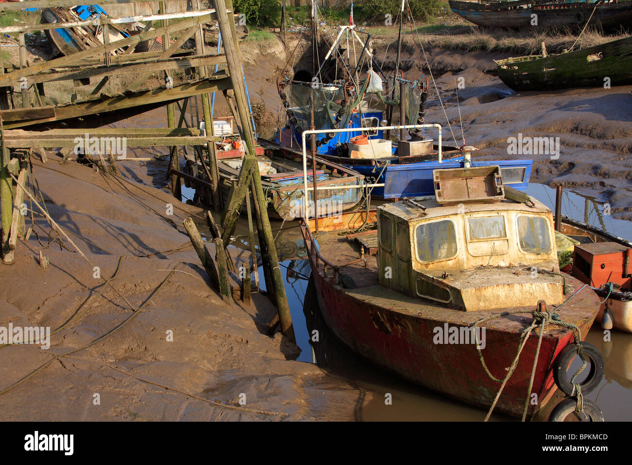 Vieux bateaux de pêche dans un terrain boueux quai adjacent à un ponton branlant en soirée sunshine, Kings Lynn, Norfolk Banque D'Images