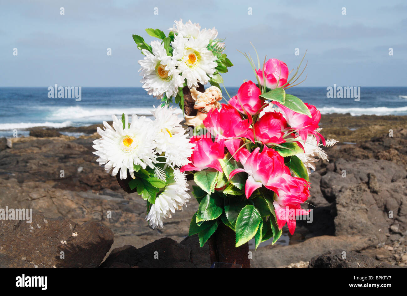 Ange et fleurs en plastique sur la croix de fer rouillée près de la mer Banque D'Images