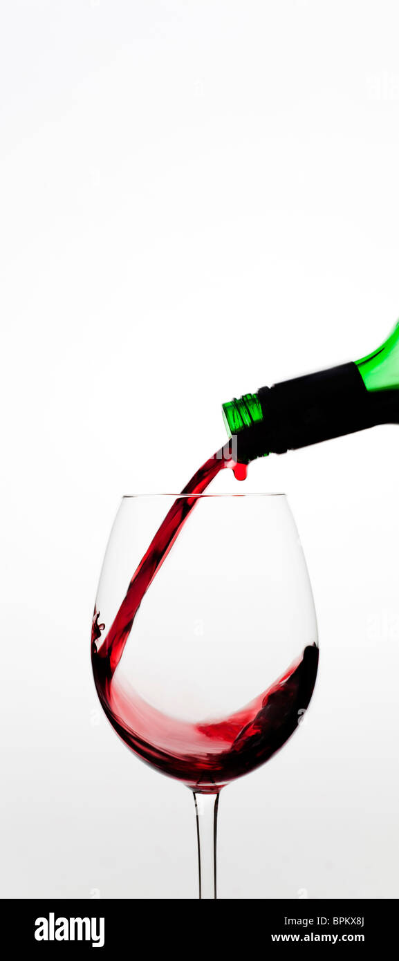 Vin rouge versé dans le verre contre fond blanc Banque D'Images