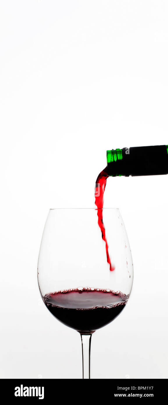 Vin rouge versé dans le verre contre fond blanc Banque D'Images