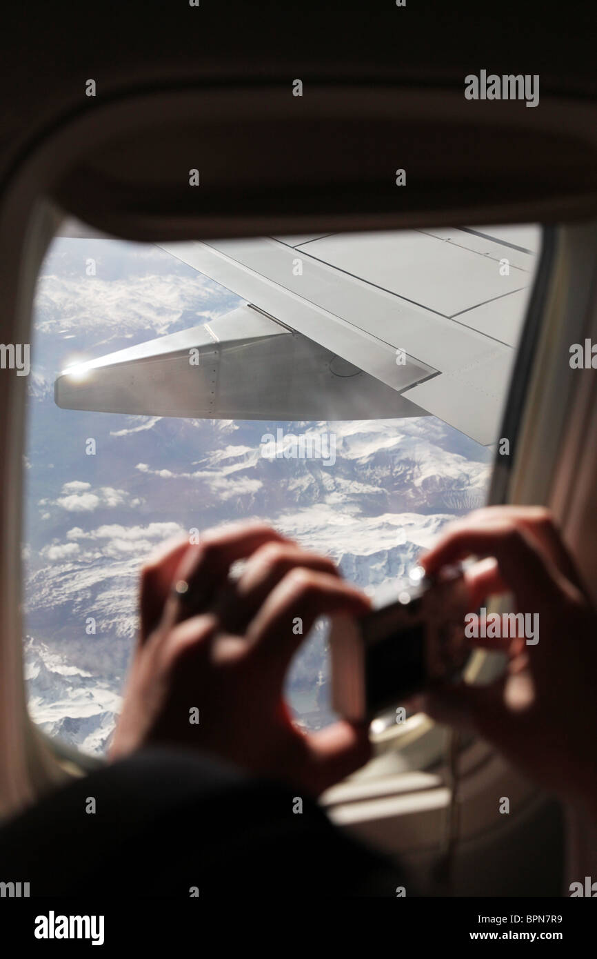Passager prend une photo des sommets enneigés des Alpes européennes en France à partir d'un avion avec un petit modèle d'appareil photo numérique libéré Banque D'Images