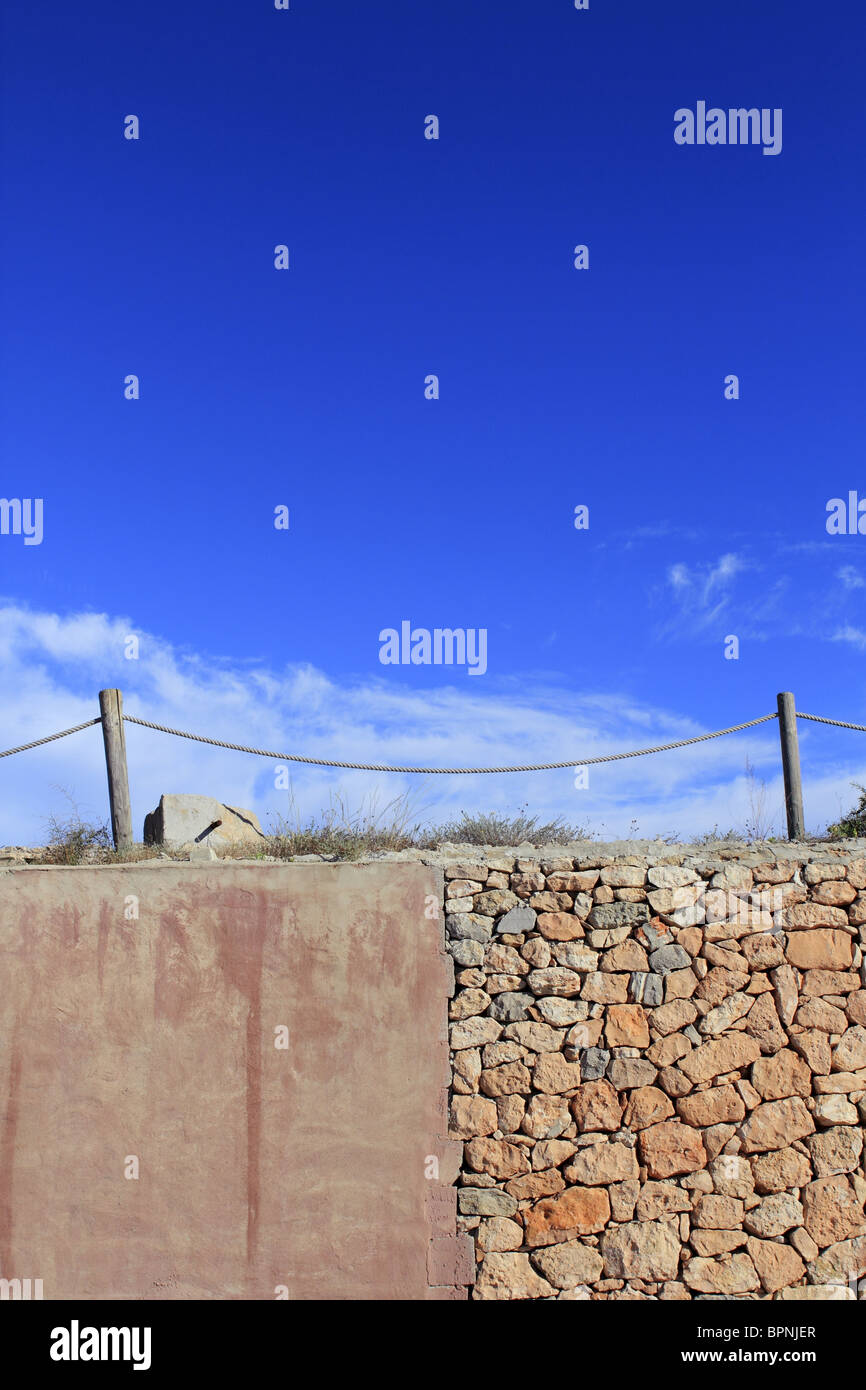 Corde traditionnel clôturer plus de mur de pierre grunge cement blue sky Banque D'Images