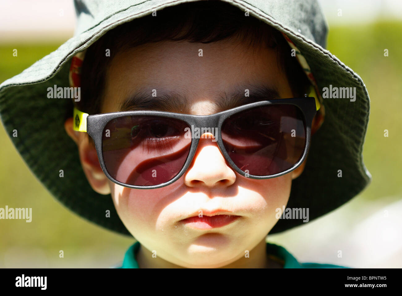 Bébé Garçon personne portant des lunettes de soleil et un grand chapeau  vert dans le soleil d'été à l'extérieur avec une expression vide Photo  Stock - Alamy