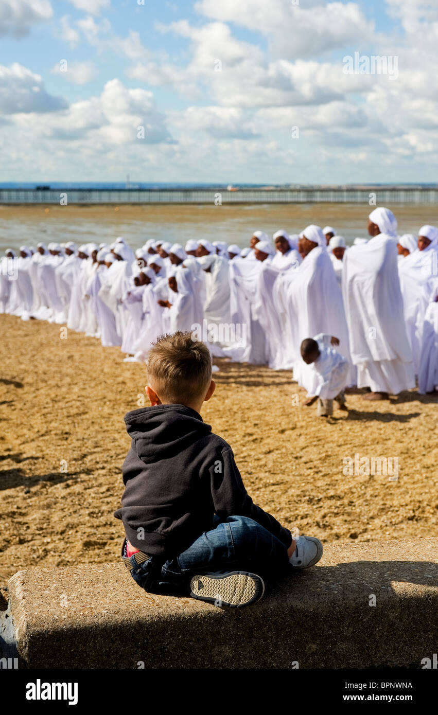 Un jeune garçon regardant des membres de l'Église des Apôtres de Muchinjikwa priant sur la plage de Jubilee à Southend. Banque D'Images