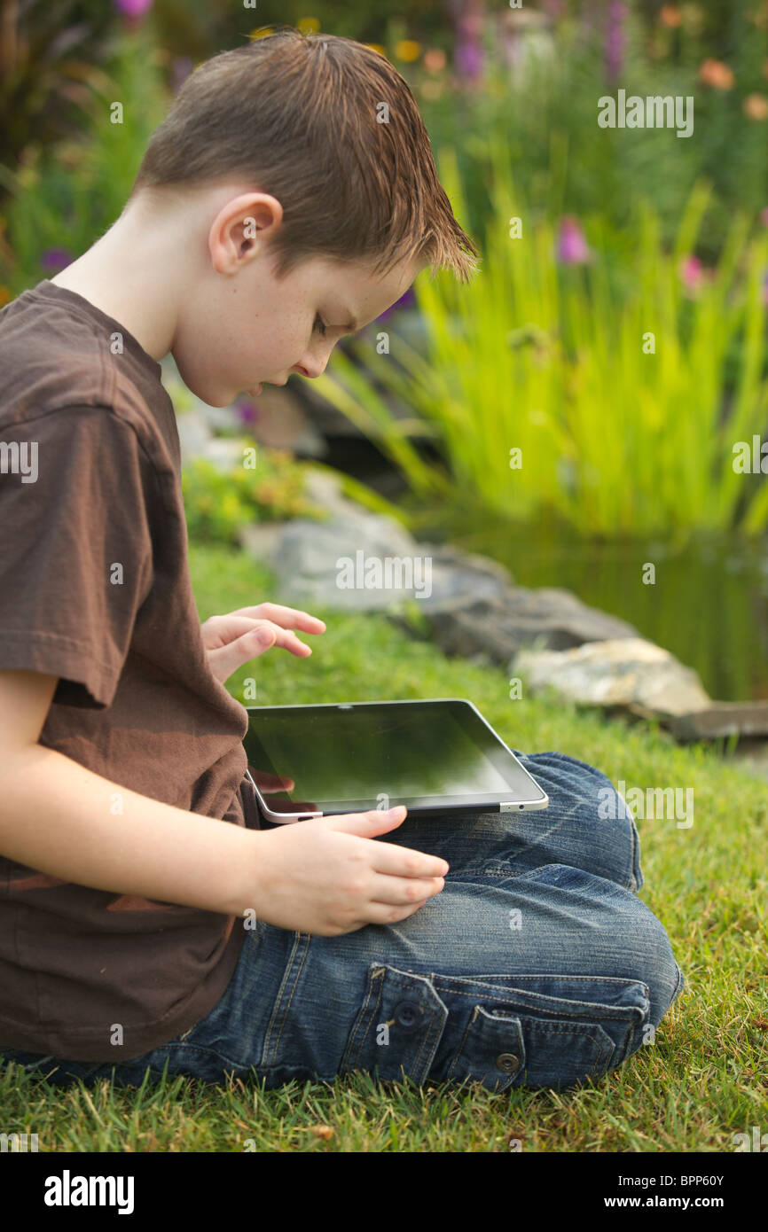 Un jeune garçon de 10 ans en utilisant un iPad dans le jardin Banque D'Images