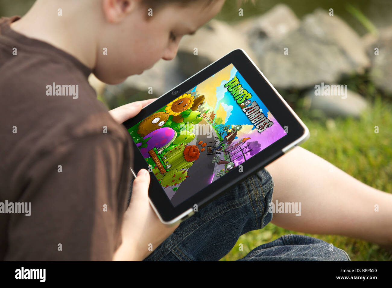 Un jeune garçon de 10 ans jouer Plantes contre zombies jeu sur un iPad dans le jardin Banque D'Images