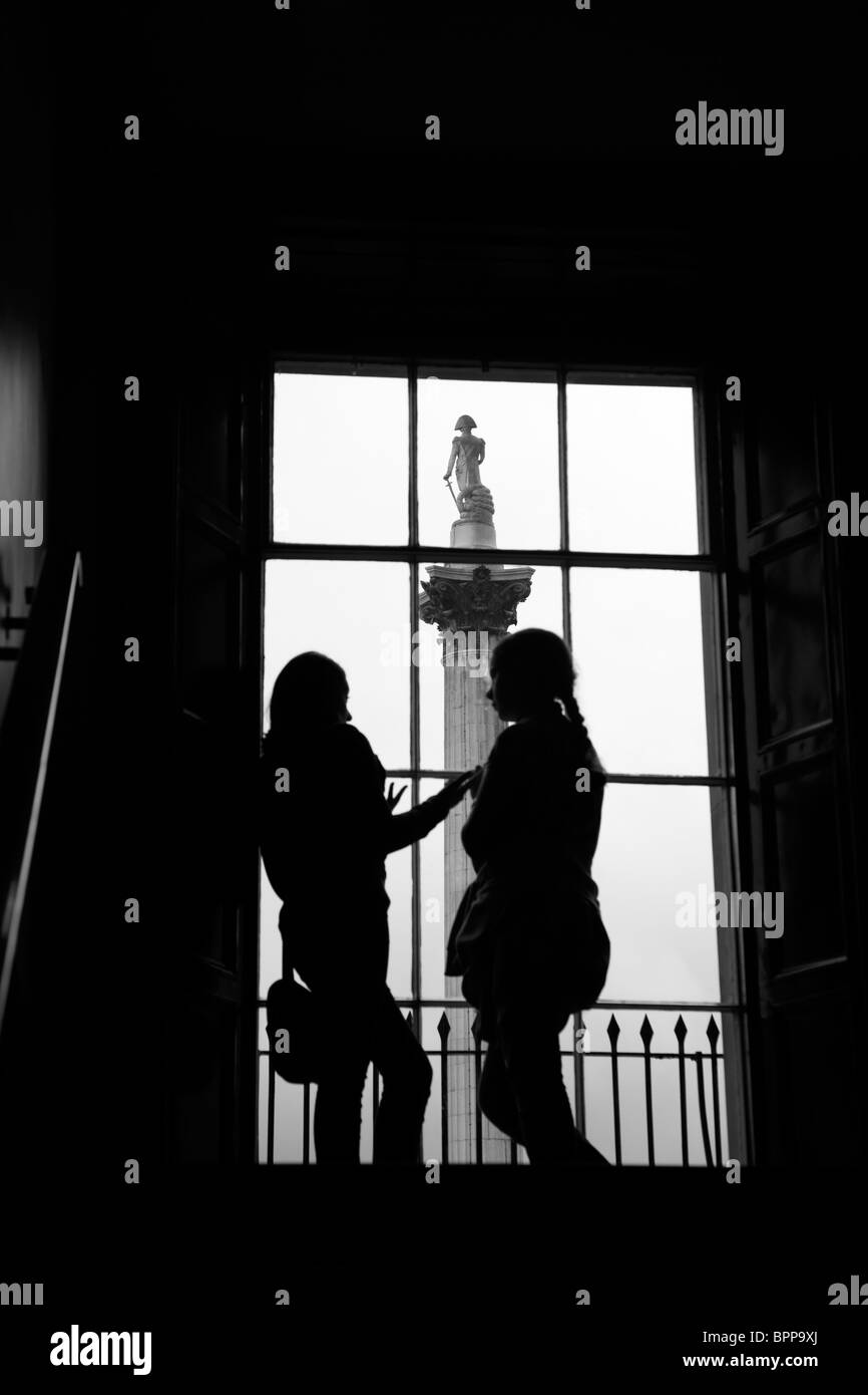 Un couple de touristes regardent par la National Gallery windows pour la Colonne Nelson, Trafalgar Square, Londres, UK Banque D'Images