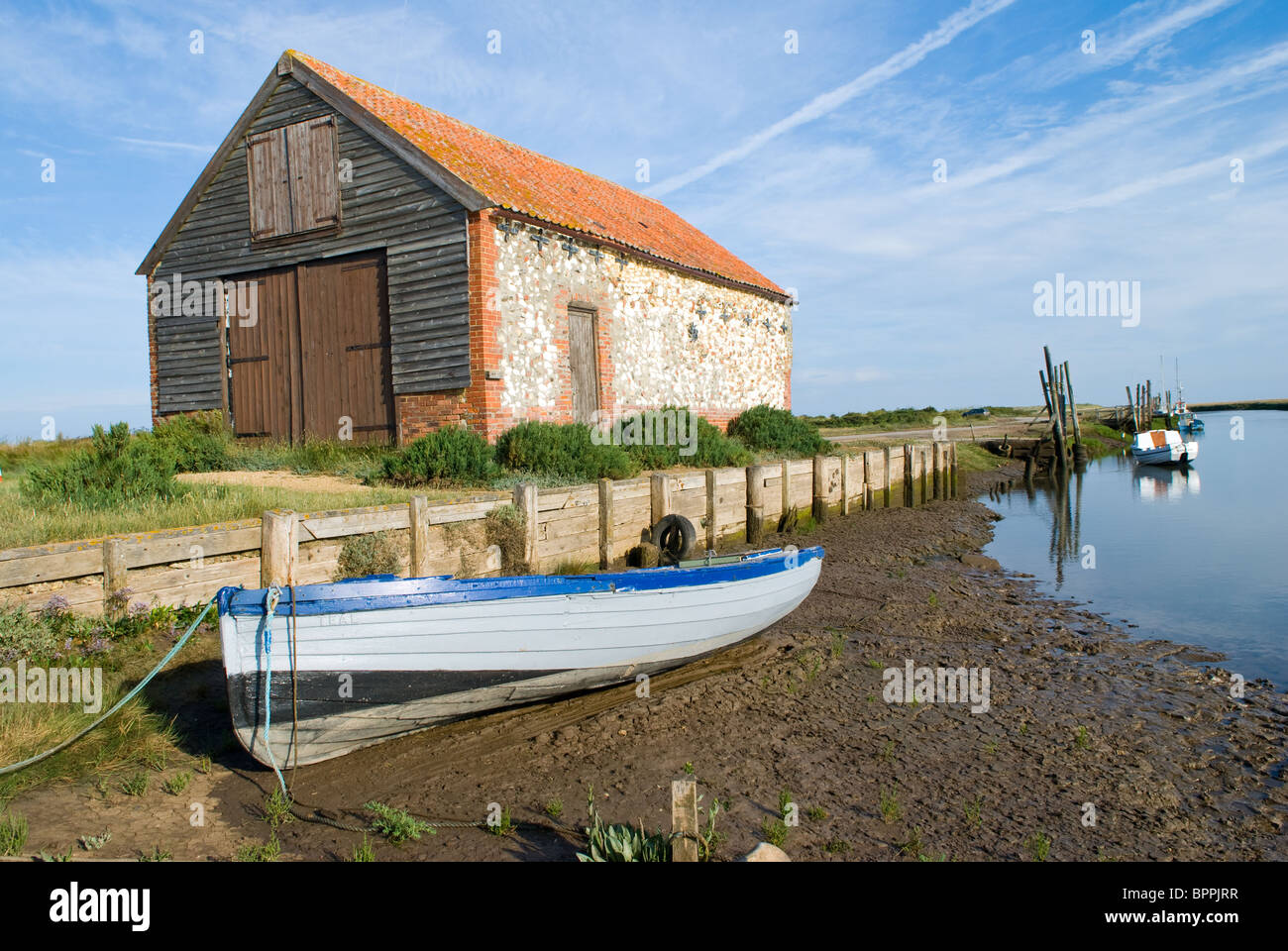 Planches en bois traditionnel bateau à rames à gauche sur des vasières à marée basse avec bâtiment de stockage avec en arrière-plan Banque D'Images