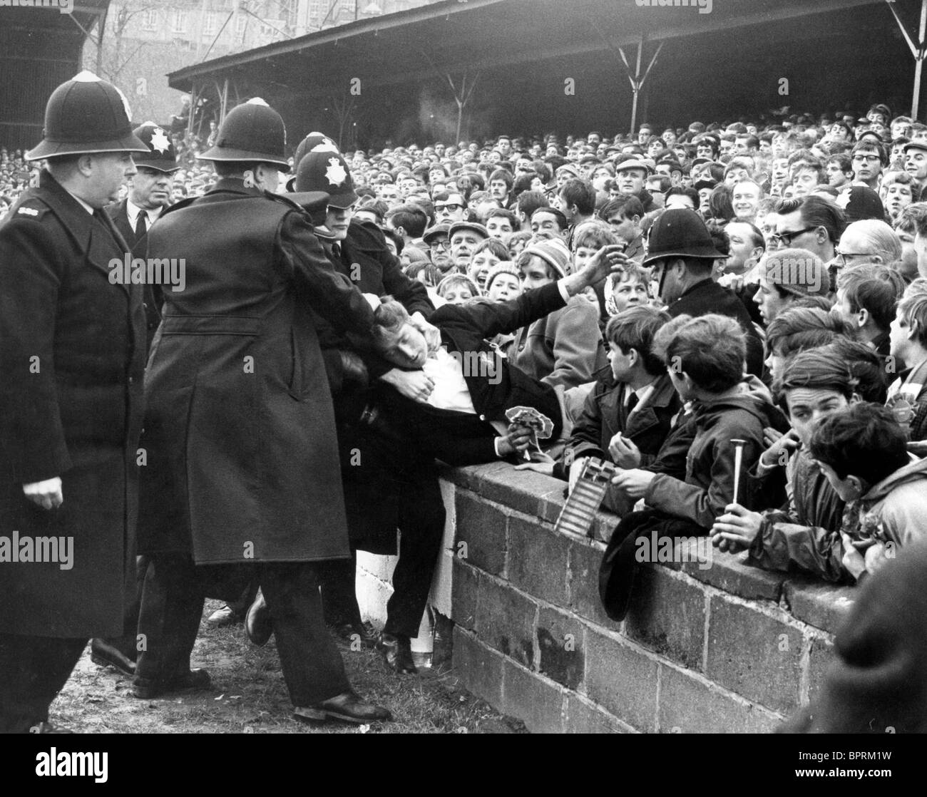 La foule de football peine la Grande-Bretagne des années 1960. Shrewsbury Town V Arsenal FA Cup Match au gay Meadow 27/1/68 des policiers retirent un supporter d'Arsenal de la PHOTO de David BAGNALL Banque D'Images