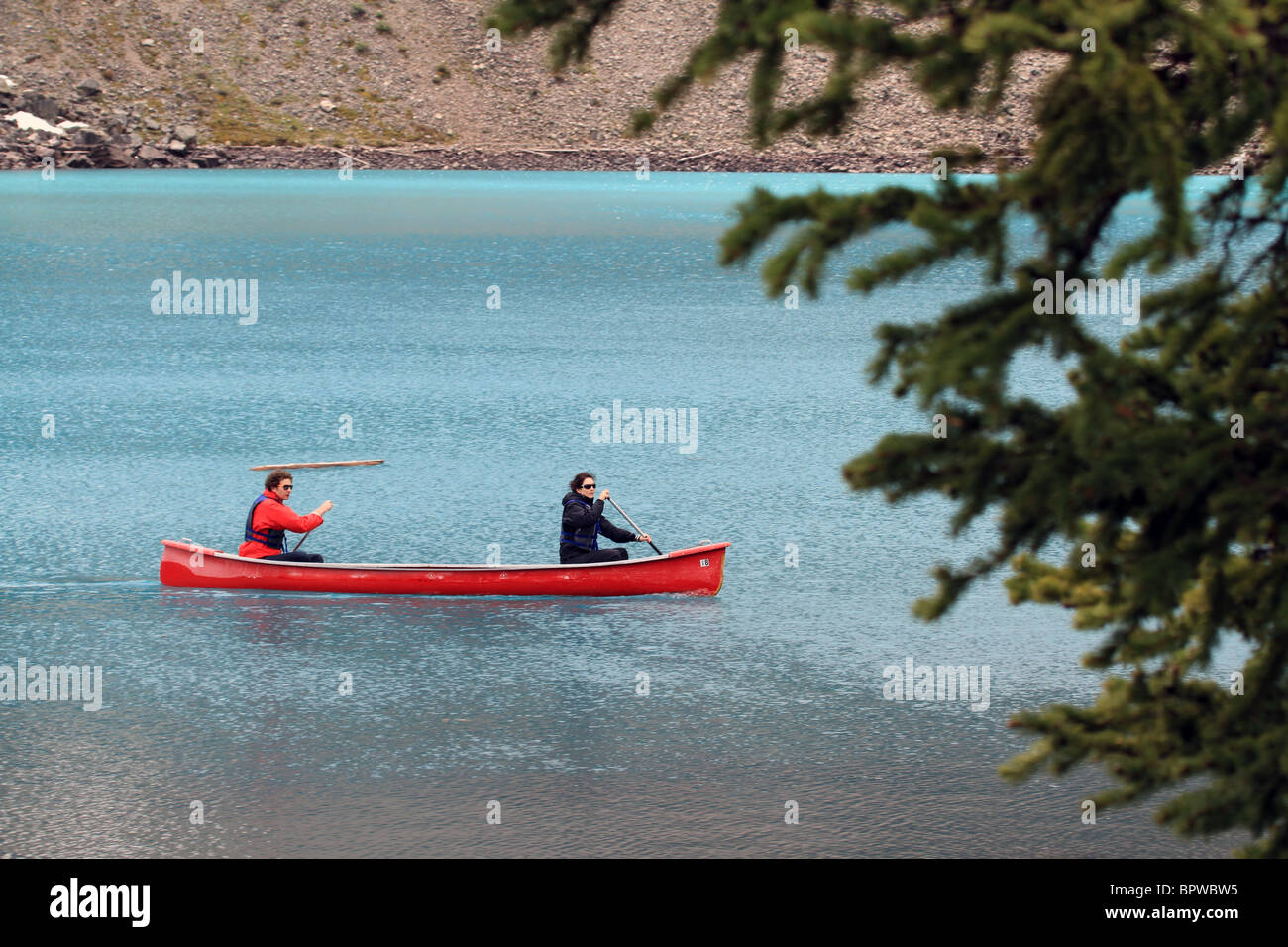 Un couple paddling canoe rouge vif sur un lac Canadien alimentés par les glaciers. Banque D'Images