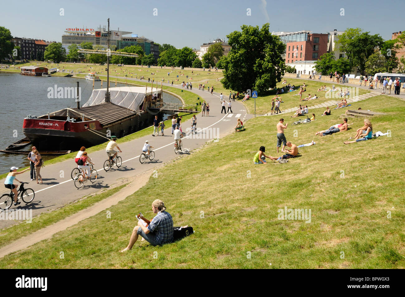 Avec une vue sur la rivière Vistule et cycliste personnes détente sur la grassy bank près de la colline de Wawel à Cracovie Banque D'Images