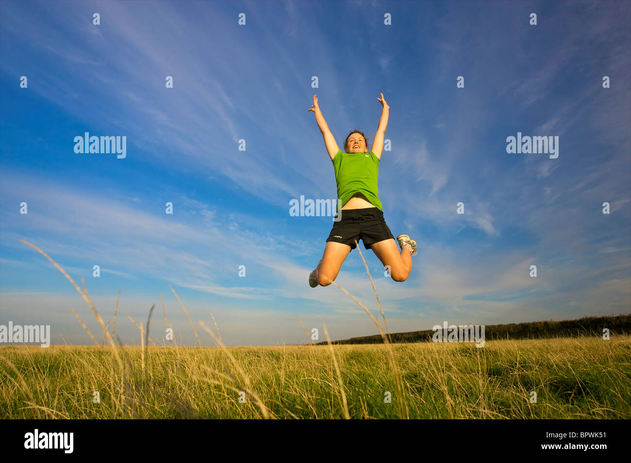 Une femme sportive, pleine d'énergie saute en l'air sur une magnifique journée d'été Banque D'Images