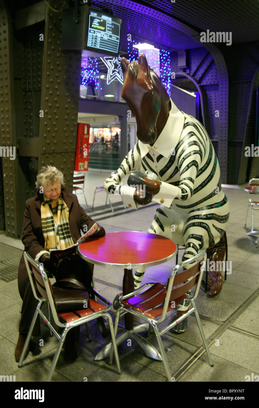 Femme à une table de café avec un cheval en vêtements zébrés, gare de Bruxelles, Belgique Banque D'Images